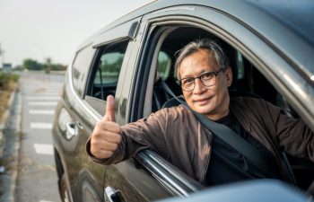 Senior Asian man drives a car vehicle on a clear day. With beautiful blue sky. He smiling driving to travel by car. Old man getting new car.